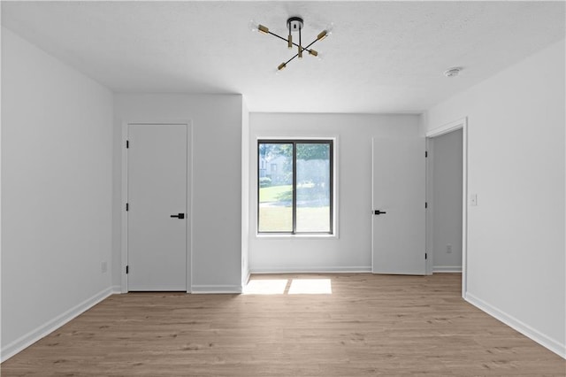 empty room featuring a notable chandelier and light hardwood / wood-style flooring