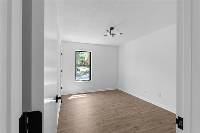 spare room featuring an inviting chandelier, dark hardwood / wood-style floors, and a textured ceiling