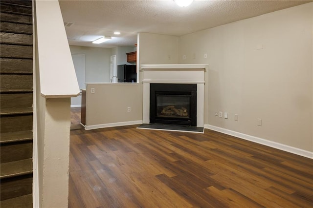 unfurnished living room featuring a textured ceiling, baseboards, stairs, dark wood-style floors, and a glass covered fireplace