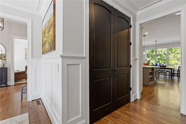 hall featuring visible vents, a decorative wall, crown molding, wainscoting, and dark wood-style flooring