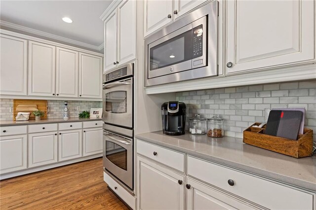 kitchen with crown molding, stainless steel appliances, light wood-style flooring, white cabinets, and backsplash