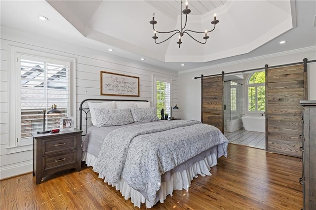 bedroom with a barn door, a raised ceiling, wood finished floors, and a notable chandelier