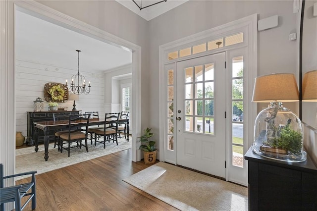 foyer with wood walls, wood finished floors, and an inviting chandelier