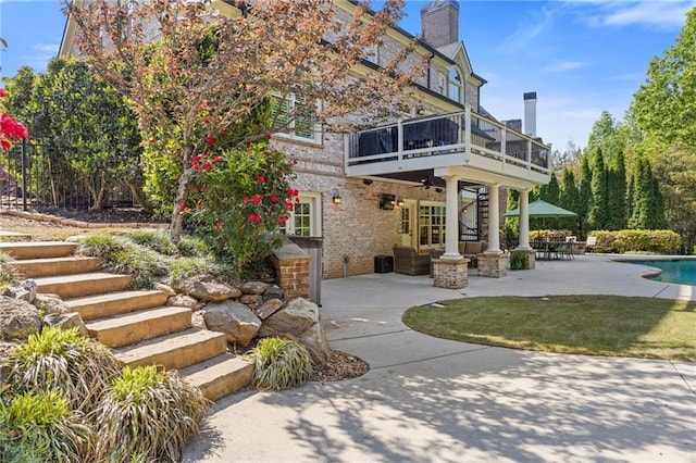 exterior space with brick siding, a patio, stairs, a balcony, and an outdoor pool