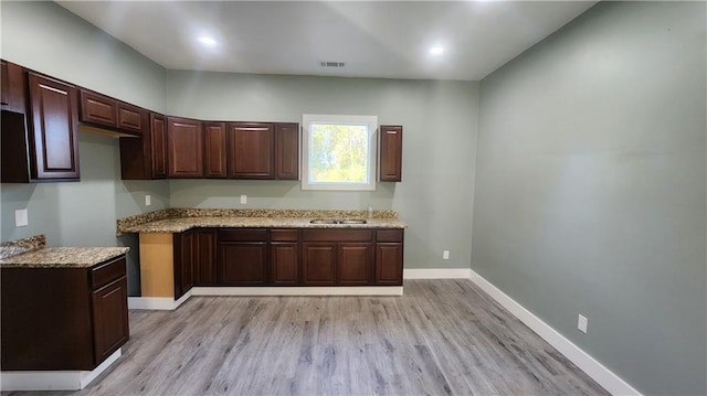 kitchen featuring light stone countertops, light wood-type flooring, dark brown cabinetry, and sink