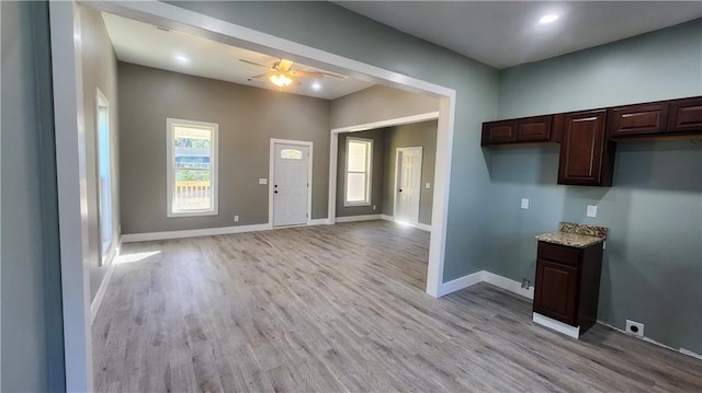 kitchen with ceiling fan, dark brown cabinets, light hardwood / wood-style floors, and light stone counters