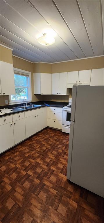 kitchen featuring dark countertops, white appliances, and white cabinetry