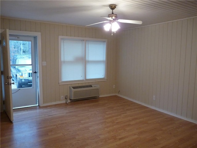 spare room featuring a ceiling fan, an AC wall unit, baseboards, and wood finished floors