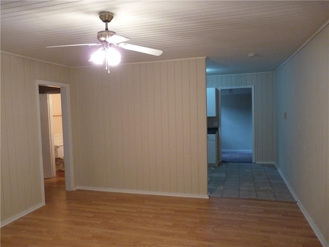 spare room featuring ceiling fan, baseboards, wood finished floors, and crown molding