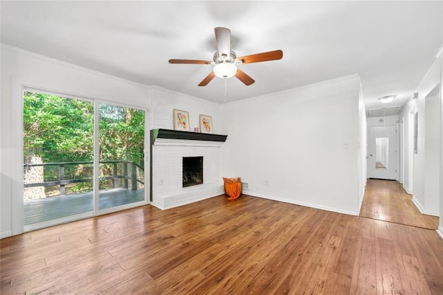 unfurnished living room featuring attic access, a fireplace, crown molding, wood-type flooring, and a ceiling fan