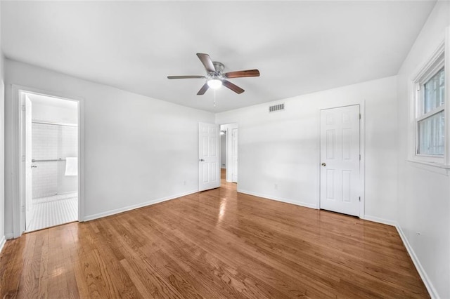unfurnished bedroom featuring a ceiling fan, baseboards, ensuite bathroom, visible vents, and wood finished floors