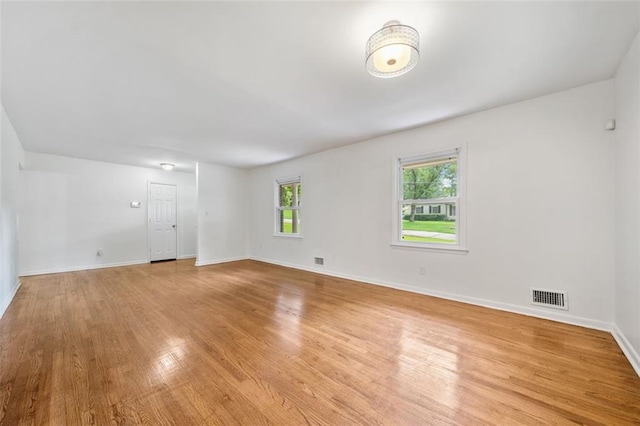 empty room with light wood-type flooring, visible vents, and baseboards