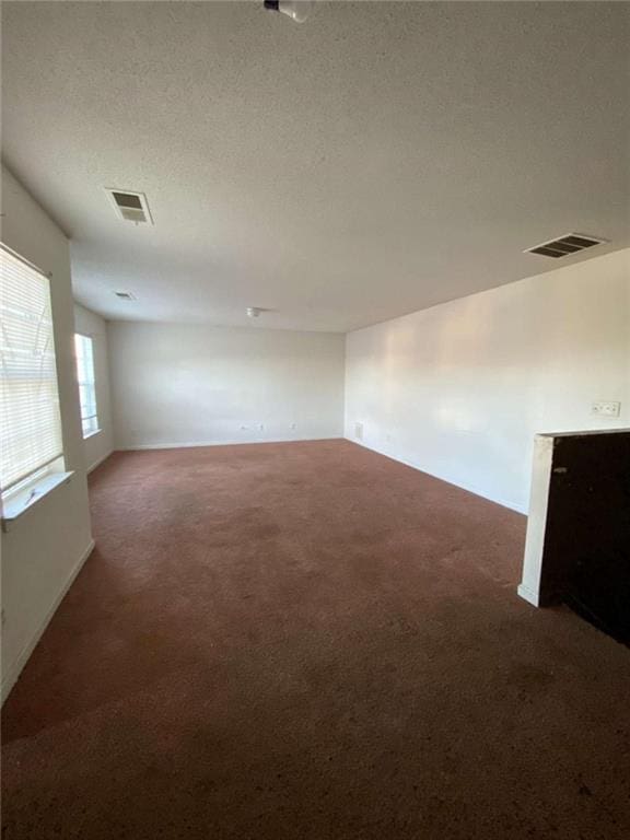 unfurnished room featuring a textured ceiling and dark colored carpet