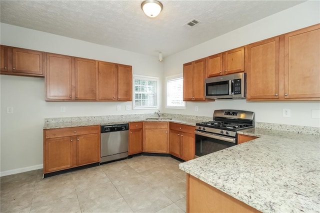 194 Wilhelmina Dr, Austell, GA 30168 - kitchen featuring appliances with stainless steel finishes, a sink, brown cabinets, light stone counters, and a textured ceiling