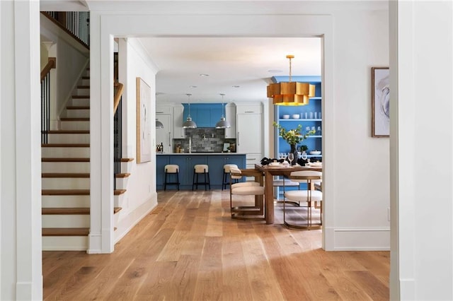 corridor with light wood-type flooring, baseboards, and stairs