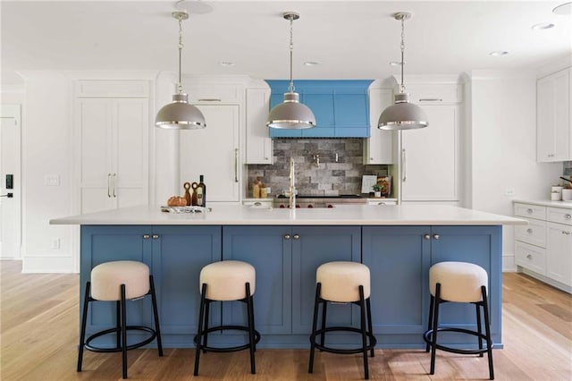 kitchen with a breakfast bar, light wood finished floors, backsplash, light countertops, and white cabinets