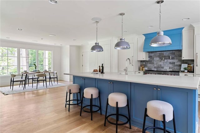 kitchen with light wood finished floors, a sink, white cabinetry, backsplash, and light countertops