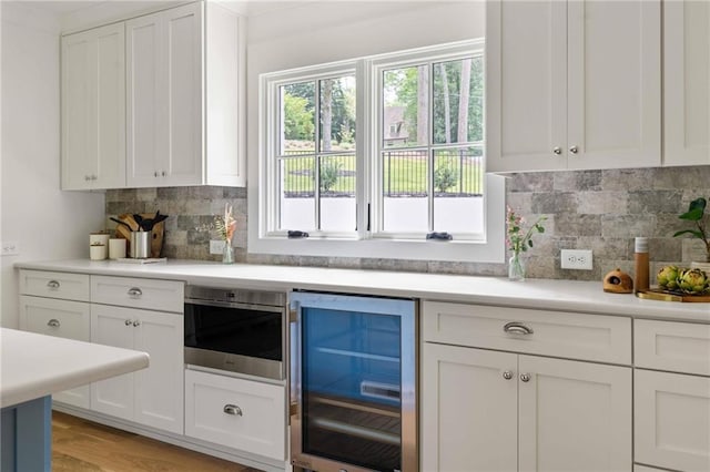 kitchen featuring backsplash, light countertops, white cabinetry, and wine cooler