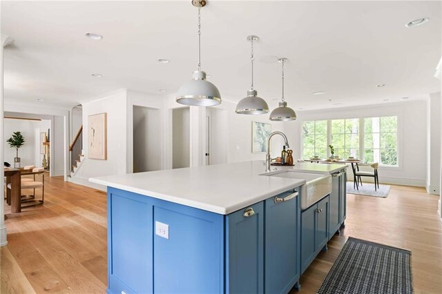 kitchen with light wood finished floors, a sink, pendant lighting, light countertops, and blue cabinetry
