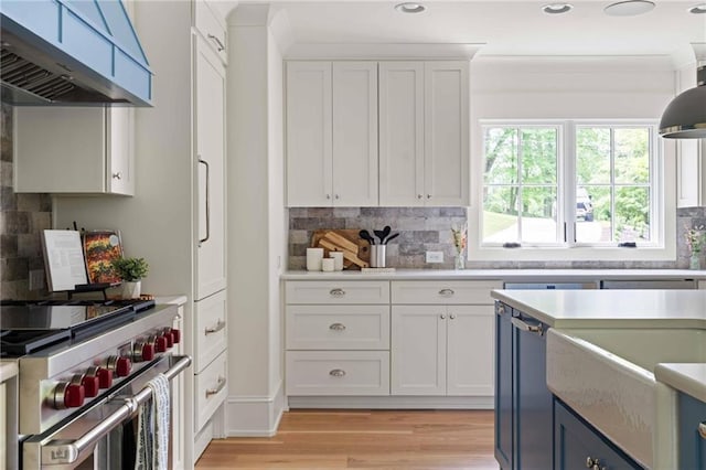 kitchen with white cabinetry, high end stainless steel range oven, light countertops, and wall chimney range hood