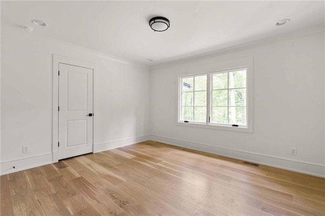 unfurnished room featuring crown molding, light wood-type flooring, visible vents, and baseboards