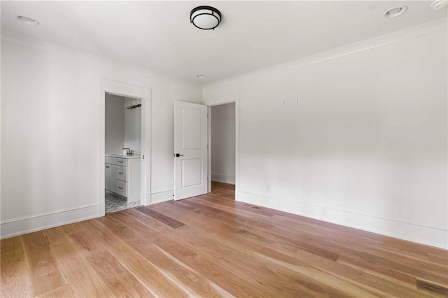 unfurnished bedroom featuring a sink, crown molding, baseboards, ensuite bath, and light wood-style floors