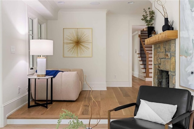 living area featuring stairs, wood finished floors, ornamental molding, a fireplace, and baseboards