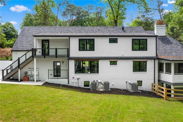 rear view of house with stairs, a chimney, a lawn, and a balcony