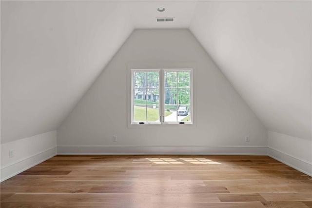 additional living space featuring light wood-type flooring, baseboards, visible vents, and vaulted ceiling