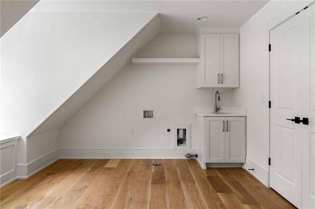 interior space featuring light wood-style flooring, indoor wet bar, electric dryer hookup, cabinet space, and a sink