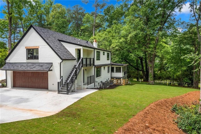 rear view of property featuring a garage, a chimney, a yard, driveway, and stairs