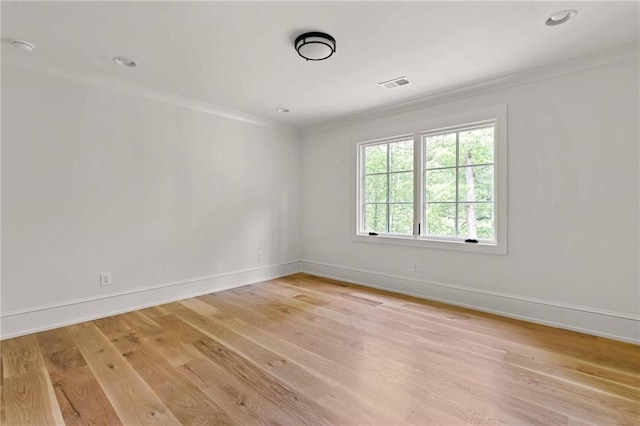 empty room with light wood finished floors, ornamental molding, baseboards, and visible vents