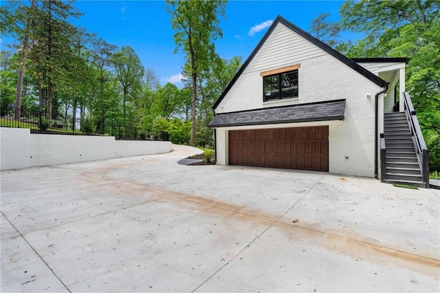 view of home's exterior featuring fence, an attached garage, brick siding, concrete driveway, and stairway
