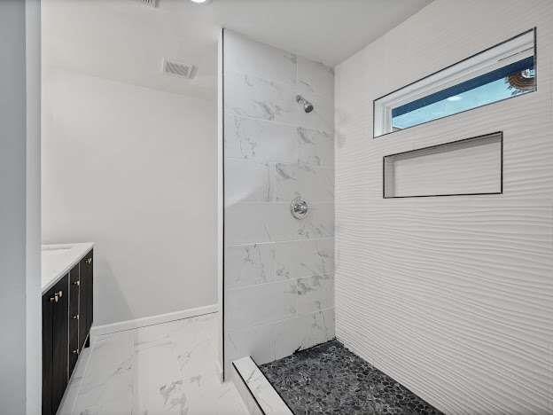 full bath with marble finish floor, tiled shower, vanity, and baseboards