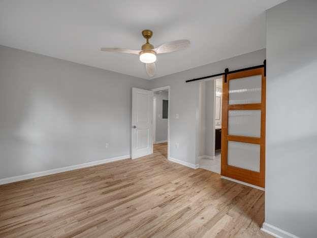 unfurnished bedroom featuring light wood finished floors, a barn door, baseboards, and ceiling fan