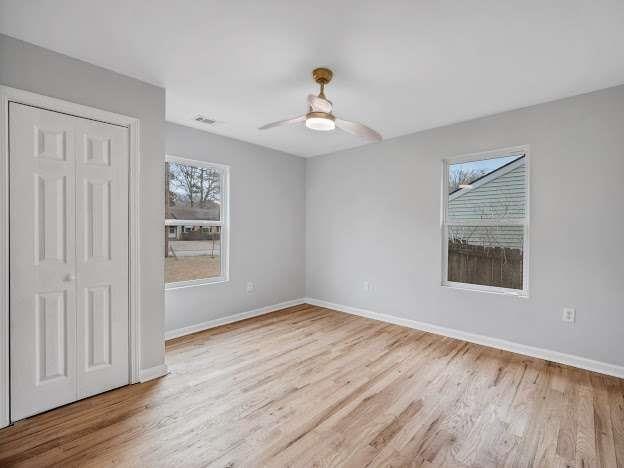 unfurnished bedroom with a closet, visible vents, ceiling fan, wood finished floors, and baseboards