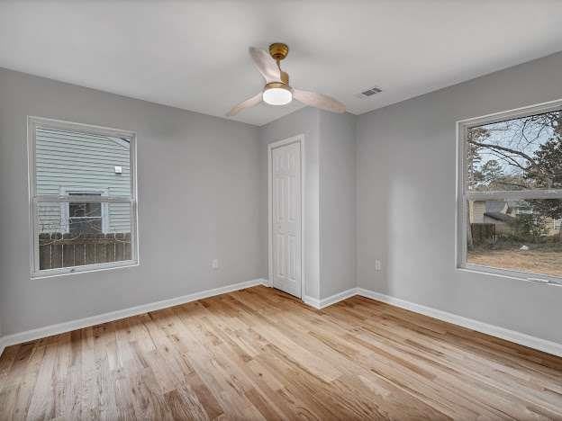 unfurnished bedroom featuring a ceiling fan, wood finished floors, visible vents, and baseboards