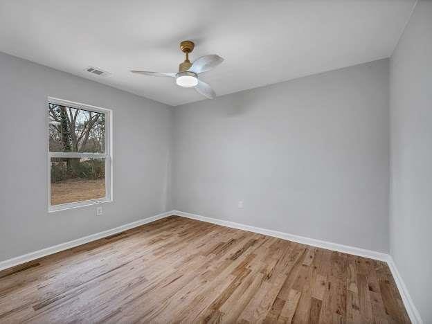 spare room with baseboards, visible vents, ceiling fan, and wood finished floors