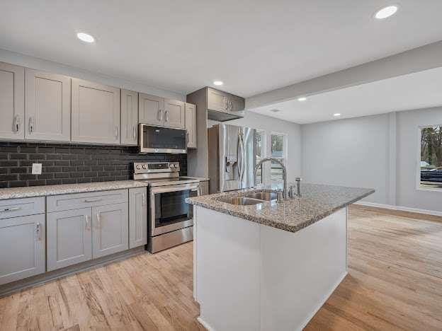 kitchen with appliances with stainless steel finishes, gray cabinets, light wood-type flooring, and a sink