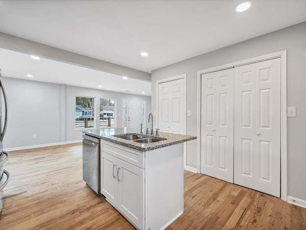 kitchen with light wood finished floors, stainless steel dishwasher, white cabinets, a sink, and light stone countertops