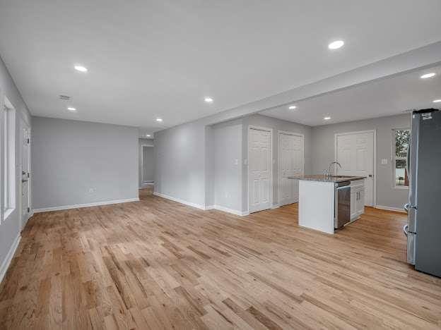 interior space with light wood finished floors, appliances with stainless steel finishes, an island with sink, and baseboards