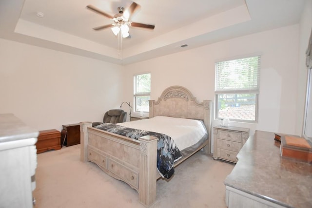 carpeted bedroom with ceiling fan, a raised ceiling, and multiple windows