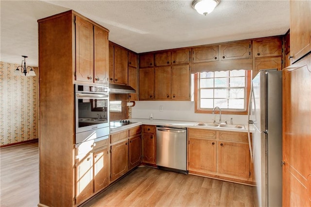 kitchen featuring light wood finished floors, brown cabinetry, stainless steel appliances, light countertops, and a sink