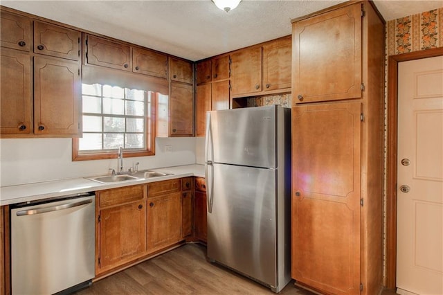 kitchen with light countertops, appliances with stainless steel finishes, a sink, and brown cabinets