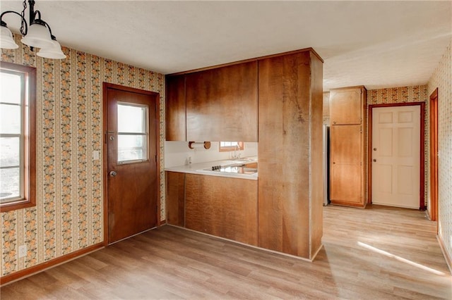 kitchen featuring pendant lighting, light countertops, light wood-type flooring, a wealth of natural light, and wallpapered walls