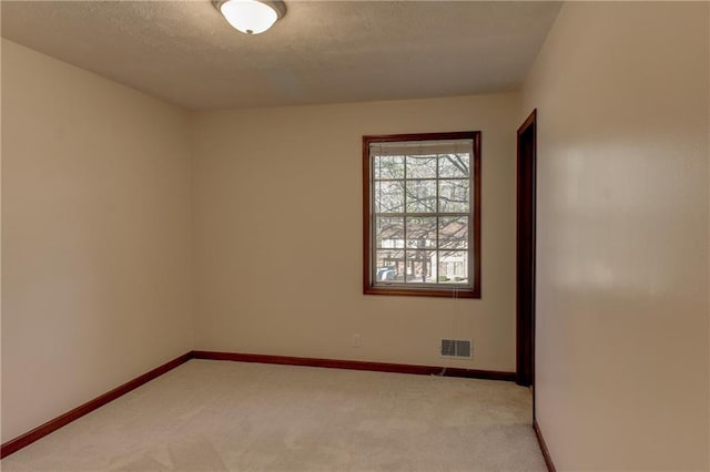 empty room featuring light colored carpet, visible vents, baseboards, and a textured ceiling