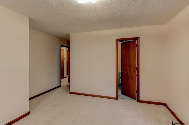 empty room featuring light colored carpet, a textured ceiling, and baseboards