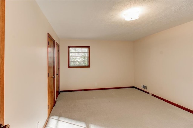 empty room featuring light carpet, baseboards, visible vents, and a textured ceiling