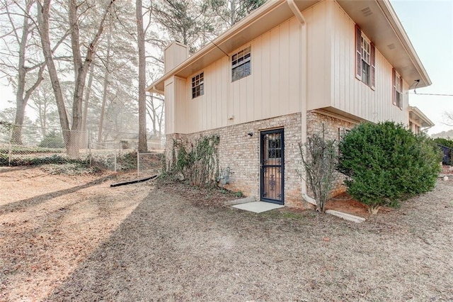 rear view of property featuring brick siding, a chimney, fence, and a gate