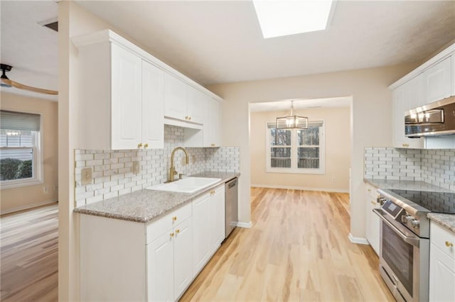 kitchen featuring sink, appliances with stainless steel finishes, light stone counters, light hardwood / wood-style floors, and white cabinets